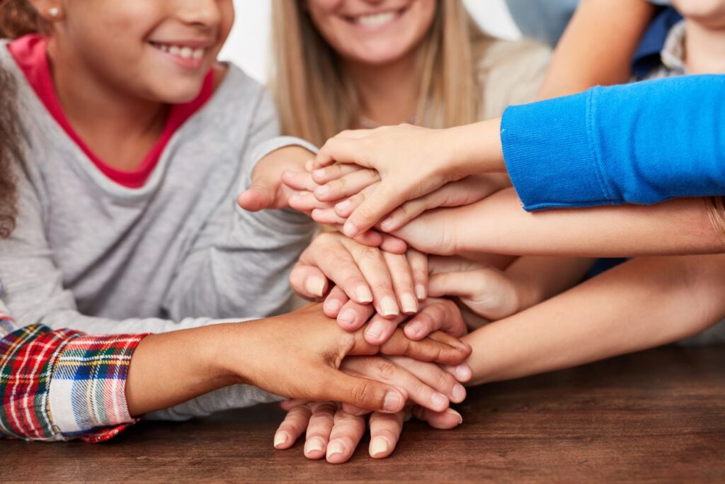 Lerntiger - Kinder stapeln Hände mit ihrer Nachmittagsbetreuerin